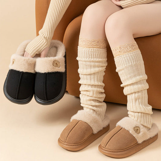 Pair of black and brown slippers held by a person wearing beige leg warmers.