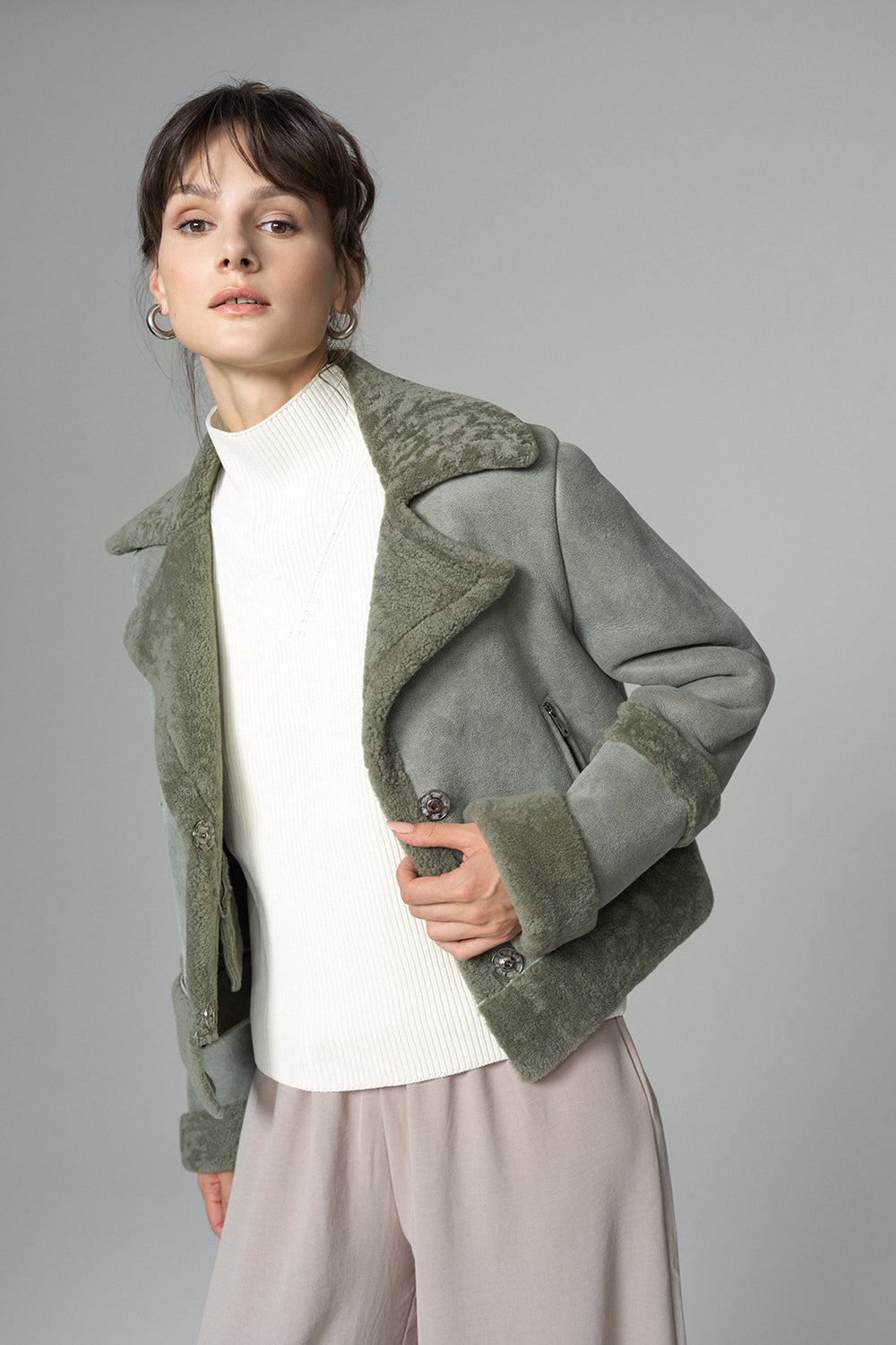 Woman wearing a green coat with fur trim on a gray background