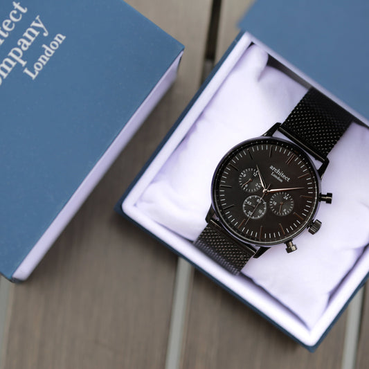 Black watch in a box with 'Company London' branding on a wooden surface