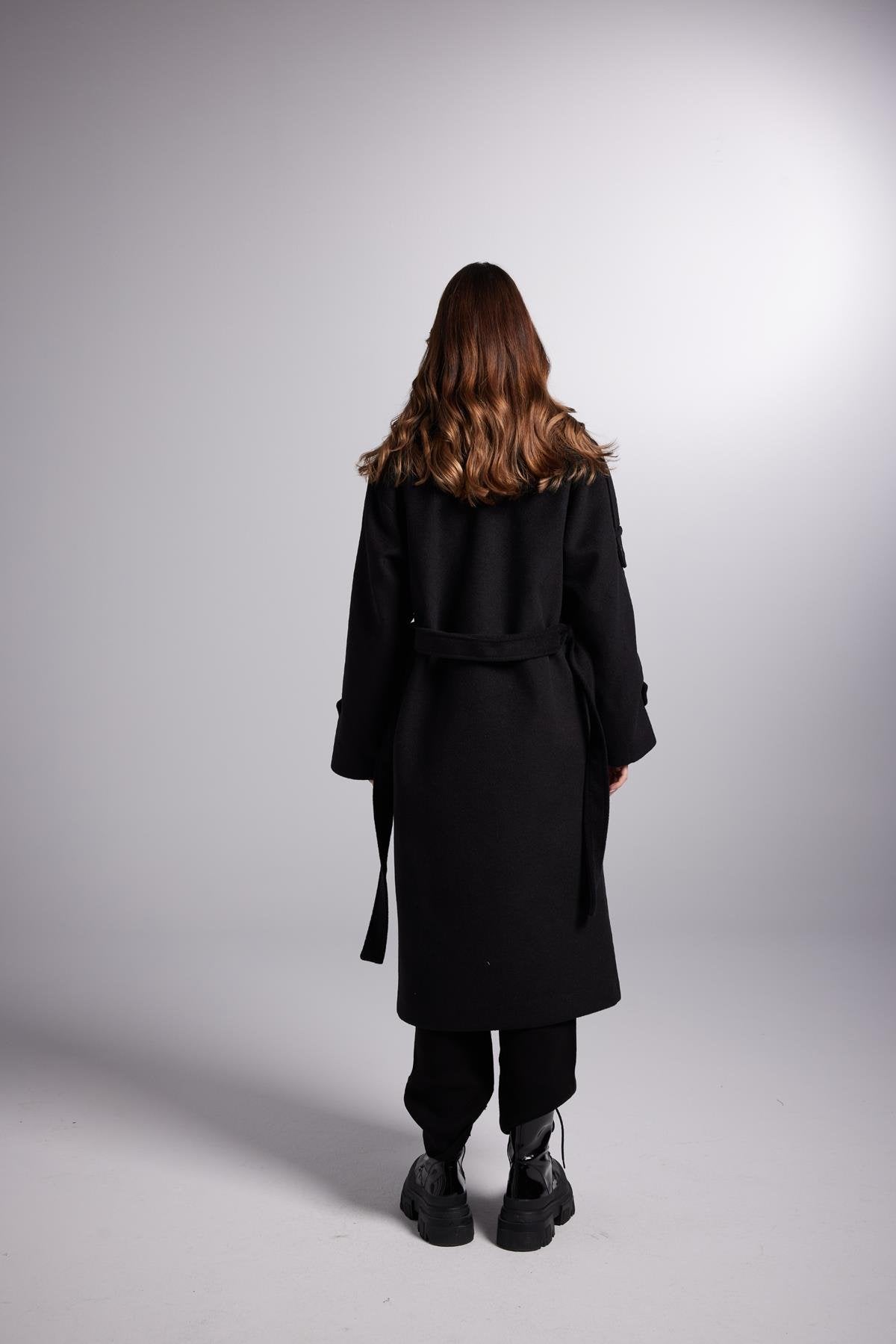 Person wearing a black coat standing against a white background