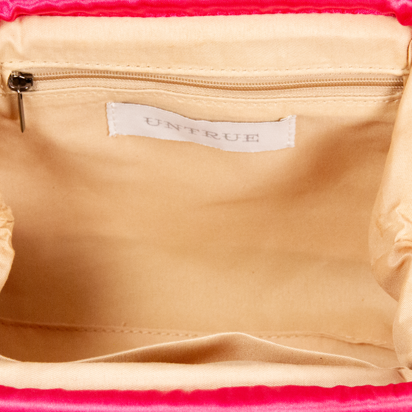 Close-up of a beige bag with a 'UNTRUE' label on a pink background