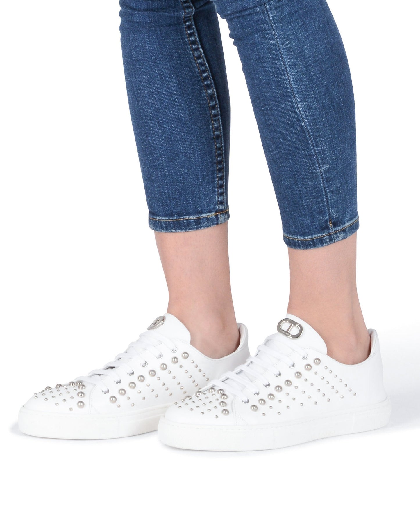 White sneakers with embellishments worn with blue jeans on a white background