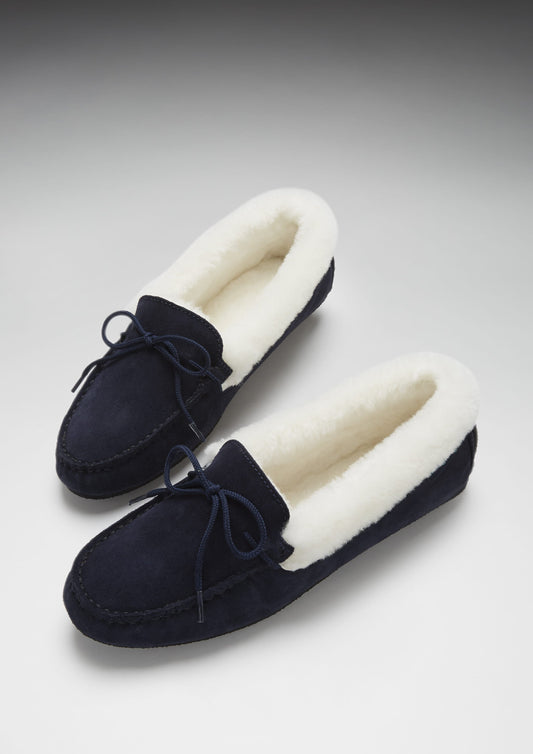 Pair of navy blue moccasin slippers with white fur lining on a light gray background