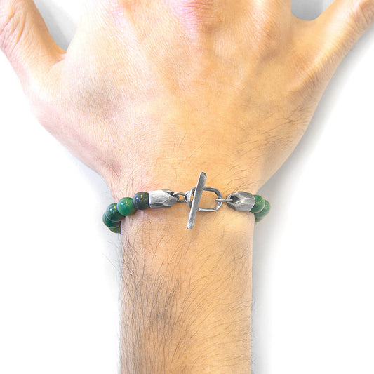 Green beaded bracelet with a silver clasp on a wrist against a white background