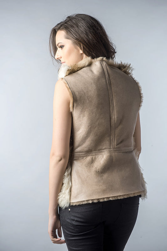 Woman wearing a brown suede vest with fur trim on a plain background