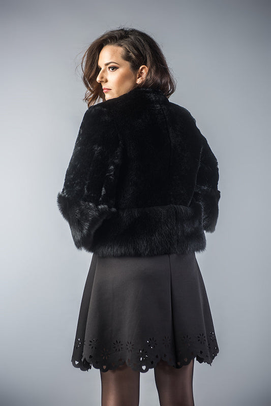Woman wearing a black fur coat and black dress against a gray background