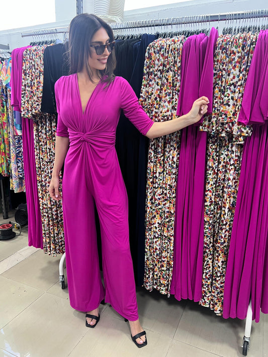 Woman in a bright pink dress standing in front of a rack of colorful dresses.