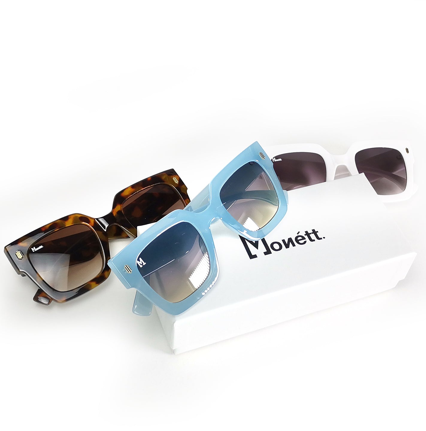 Three pairs of sunglasses on a white surface with 'Monett' branding.