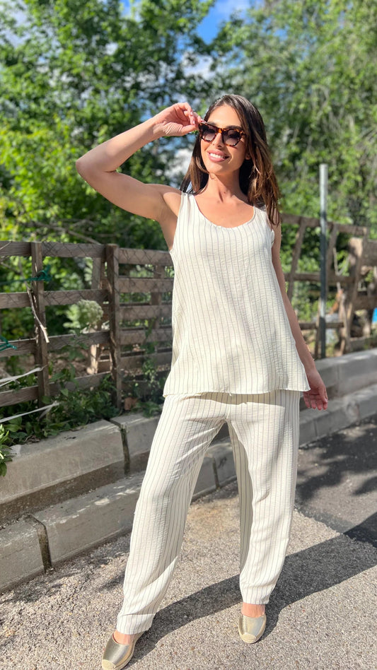 Woman in a white outfit standing outdoors with greenery in the background