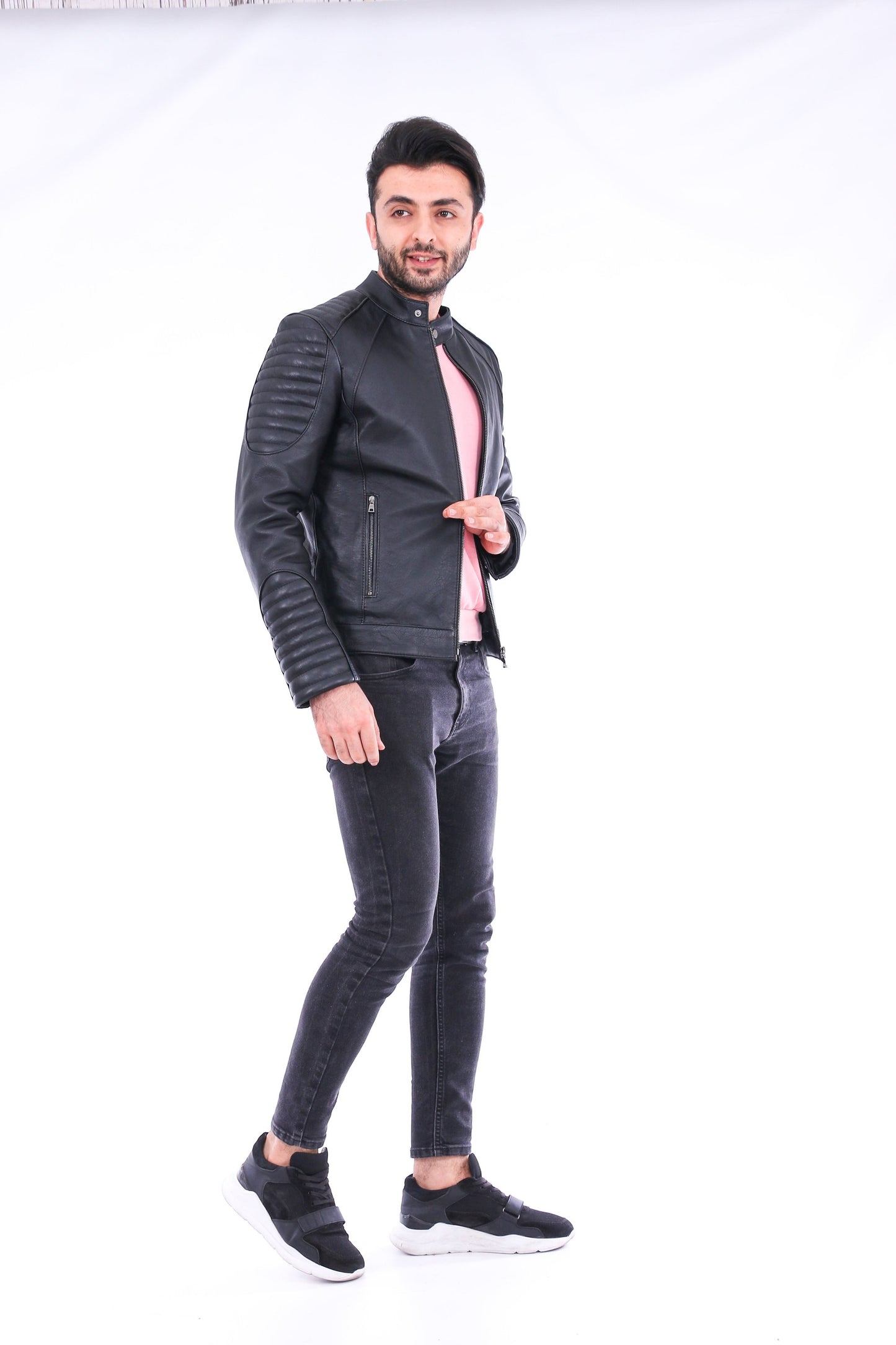 Man wearing a black leather jacket and gray jeans on a white background