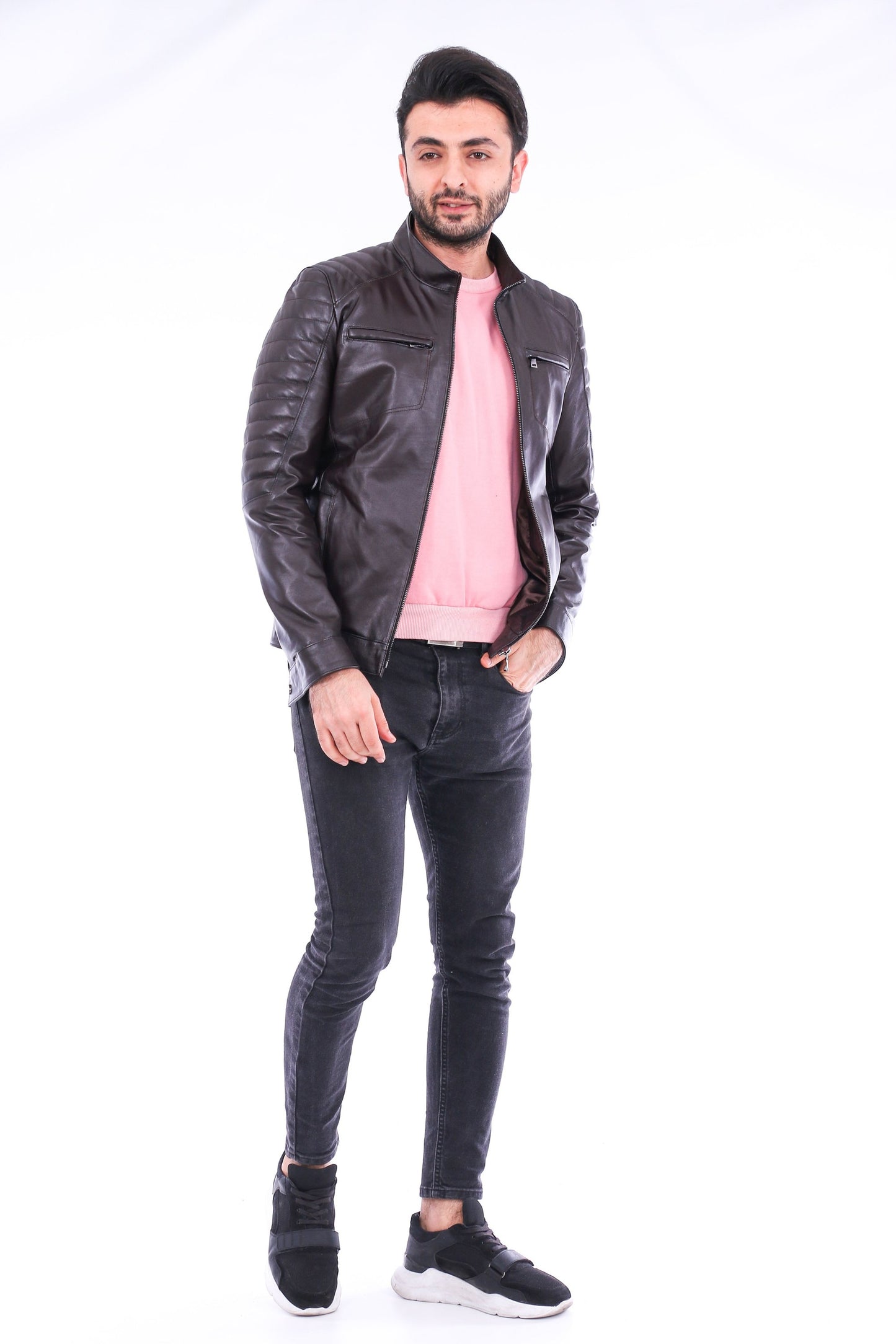 Man wearing a black leather jacket, pink shirt, and black jeans on a white background