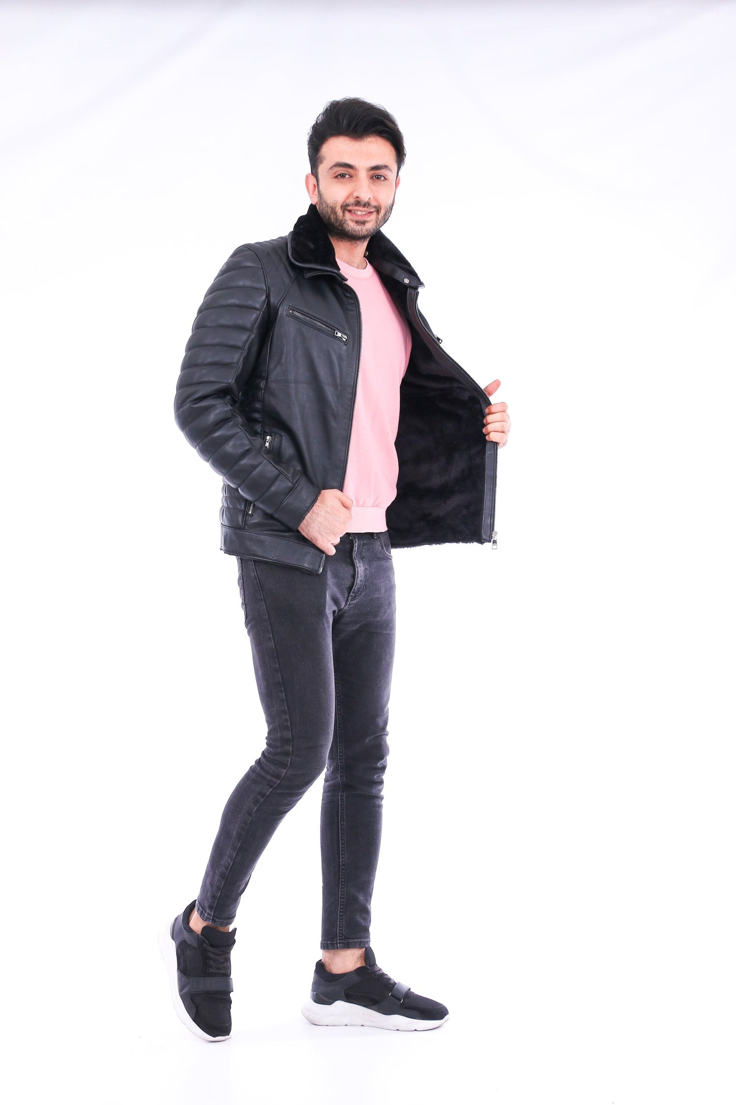 Man wearing a black jacket, pink shirt, and gray pants on a white background