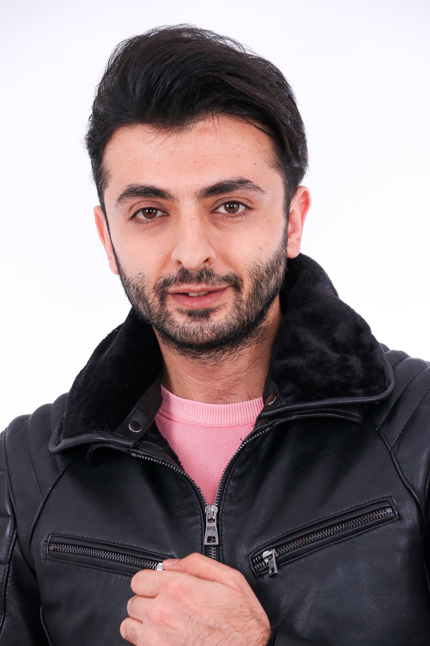 Man wearing a black leather jacket over a pink shirt on a white background