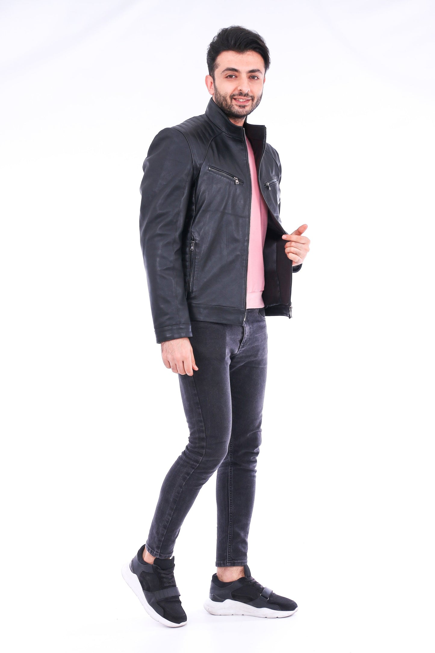 Man wearing a dark gray jacket, pink shirt, and black jeans on a white background