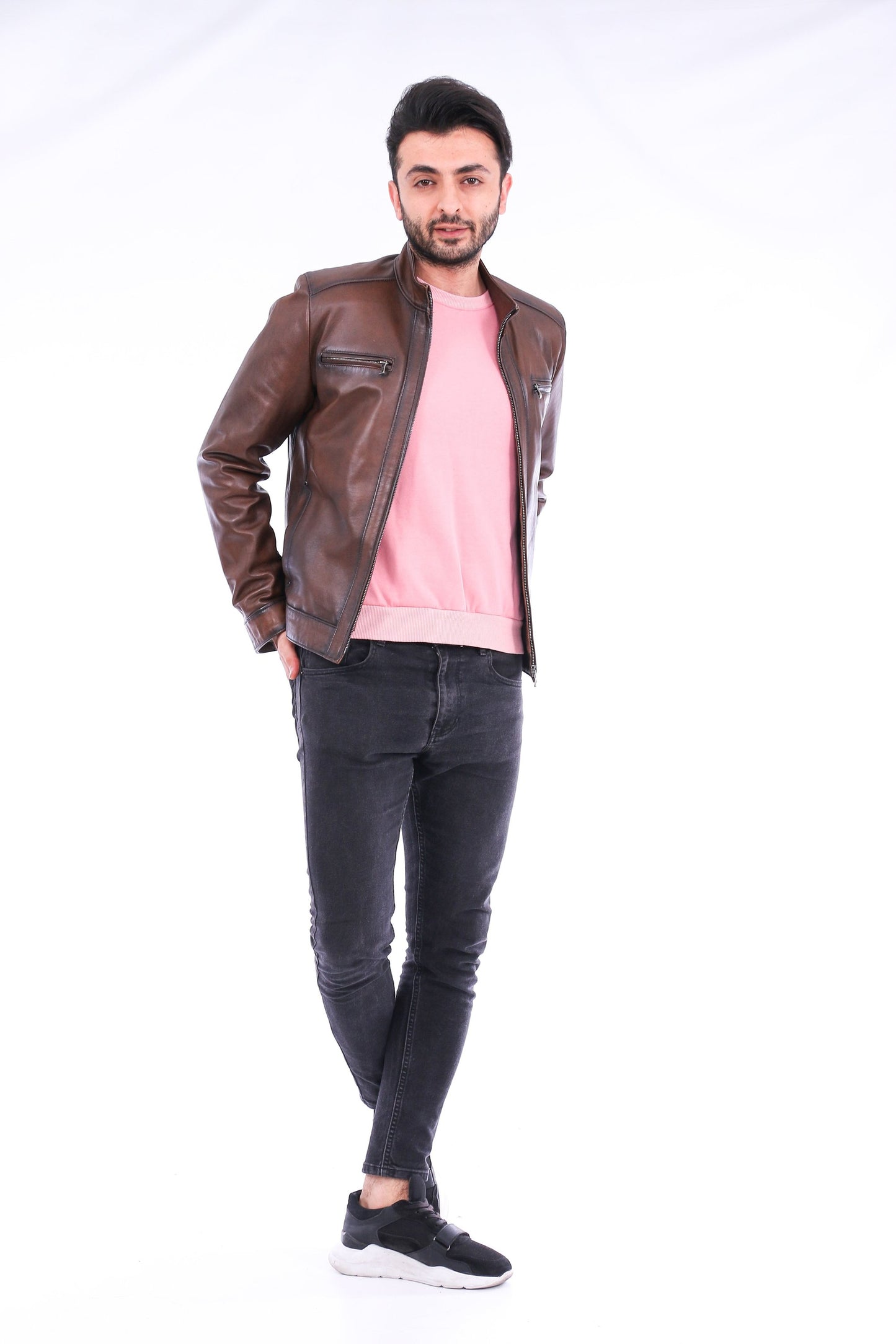 Man wearing a brown leather jacket, pink shirt, and black jeans on a white background