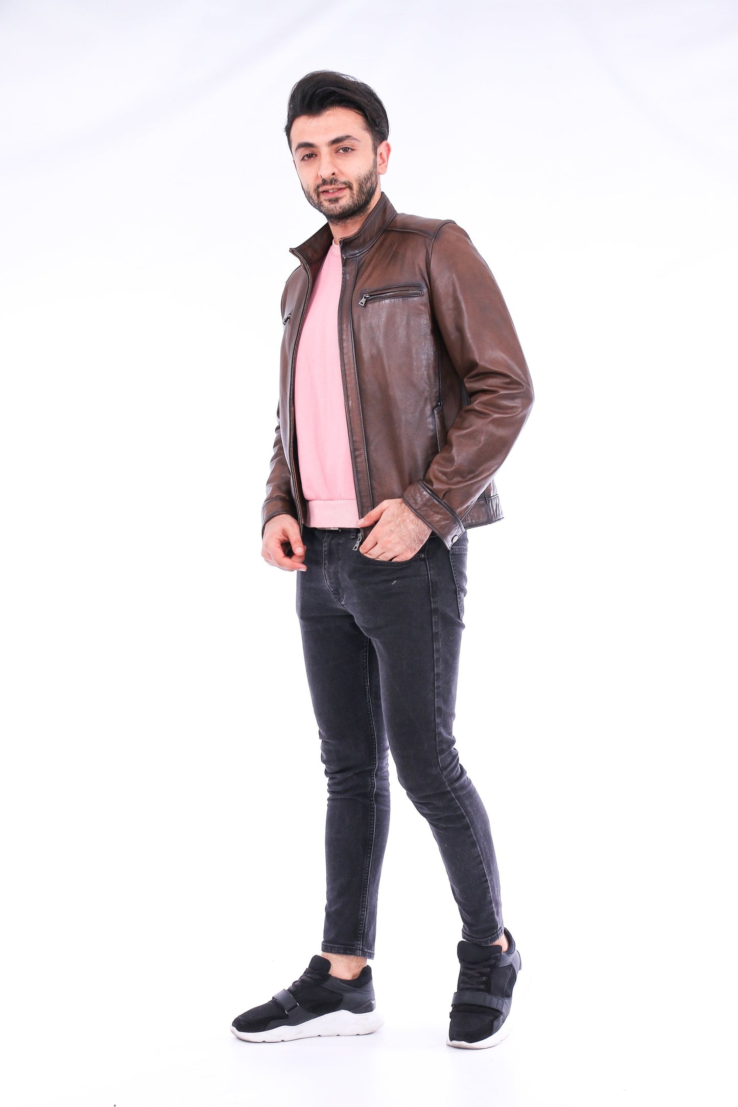 Man wearing a brown leather jacket, pink shirt, and black jeans on a white background