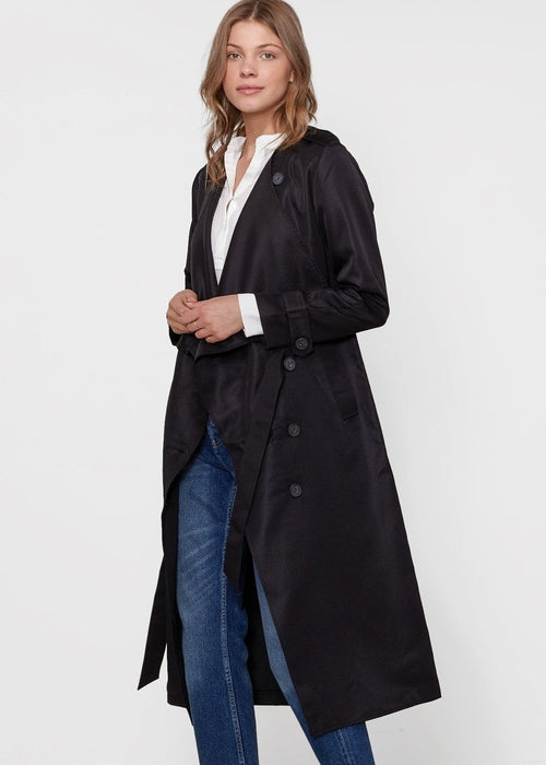 Woman wearing a black coat over a white shirt and blue jeans on a white background