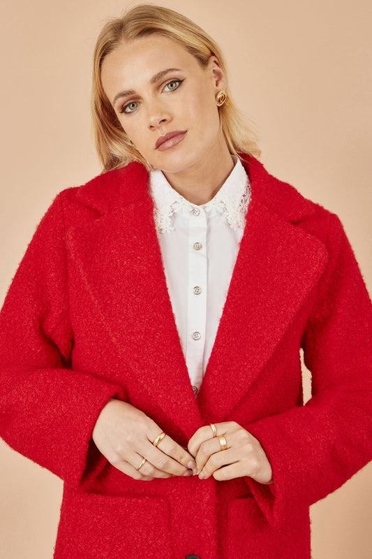 Woman wearing a red coat over a white shirt on a beige background