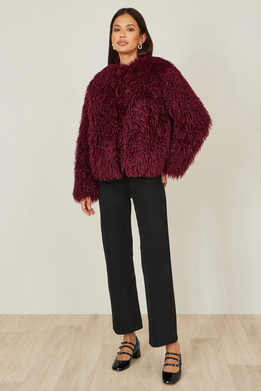 Person wearing a burgundy fluffy sweater and black pants against a white background
