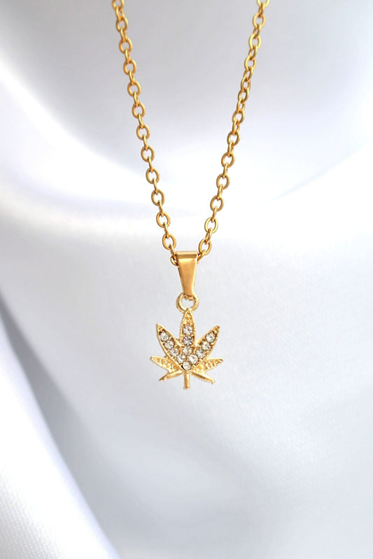 Gold necklace with a leaf-shaped pendant on a light gray background