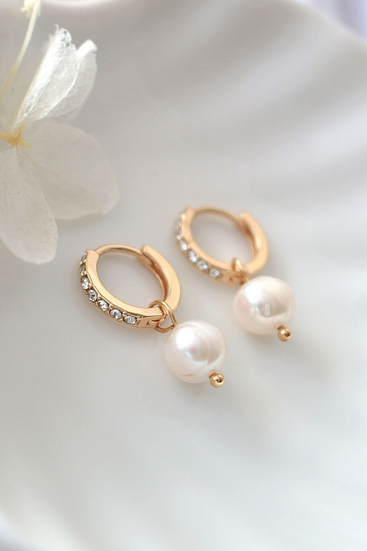 Gold hoop earrings with pearls on a white surface with flowers.