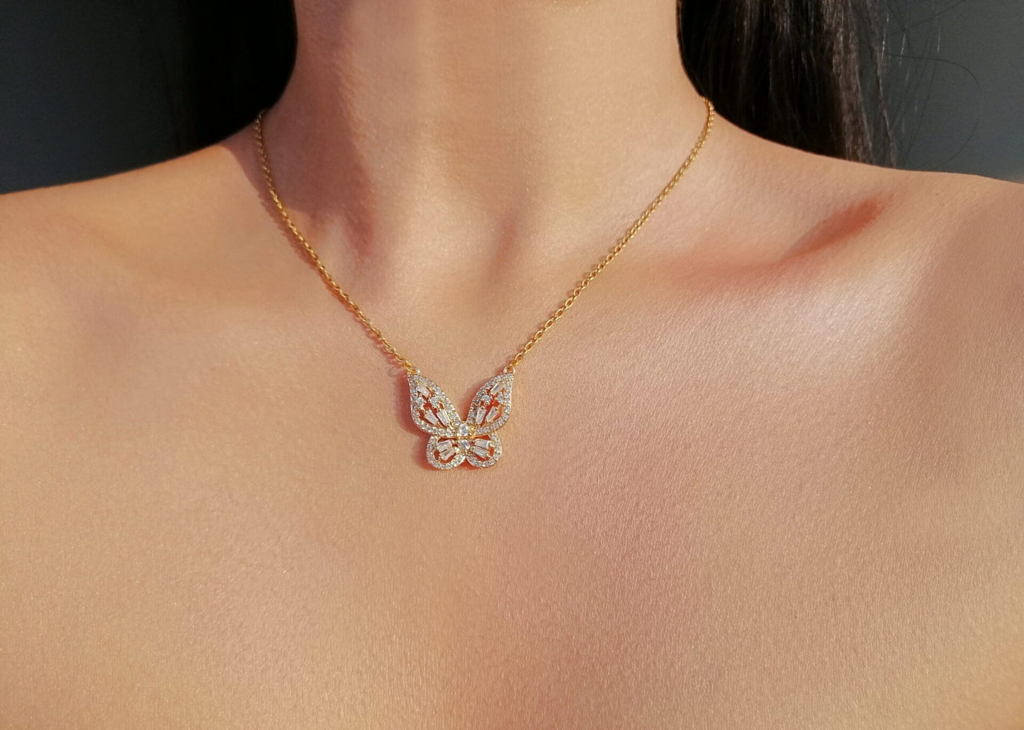 Gold necklace with a butterfly pendant on a person's neck against a dark background
