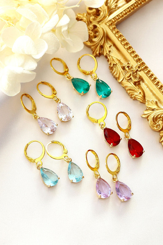 Colorful teardrop earrings with gold hooks on a white surface with decorative elements.