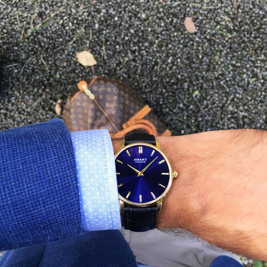Person wearing a blue and gold watch with a blue shirt sleeve outdoors.
