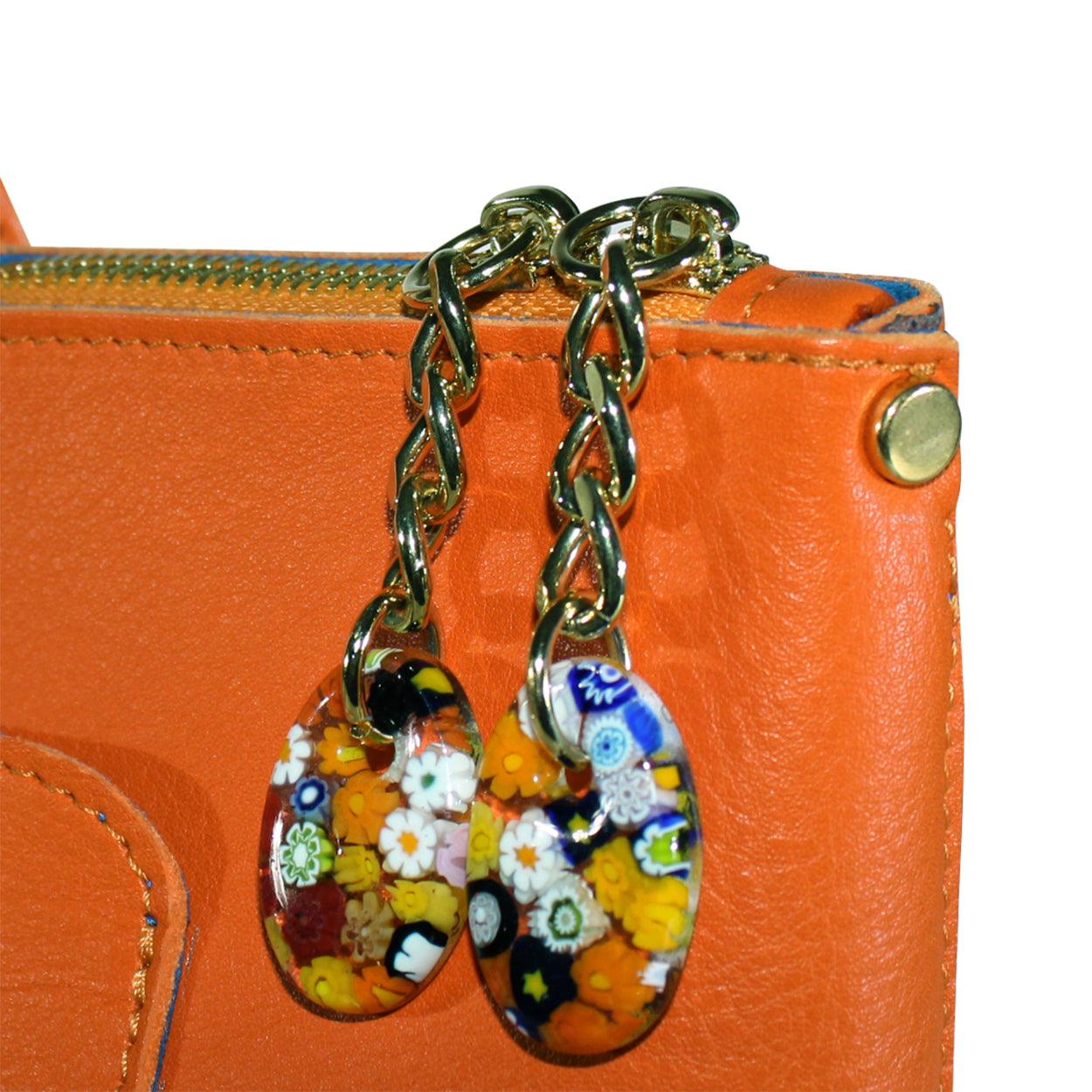 Pair of floral glass earrings on a gold chain against an orange background