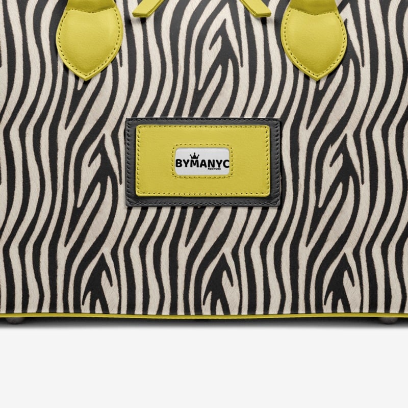 Zebra patterned bag with yellow accents and a ByManyC label on a white background