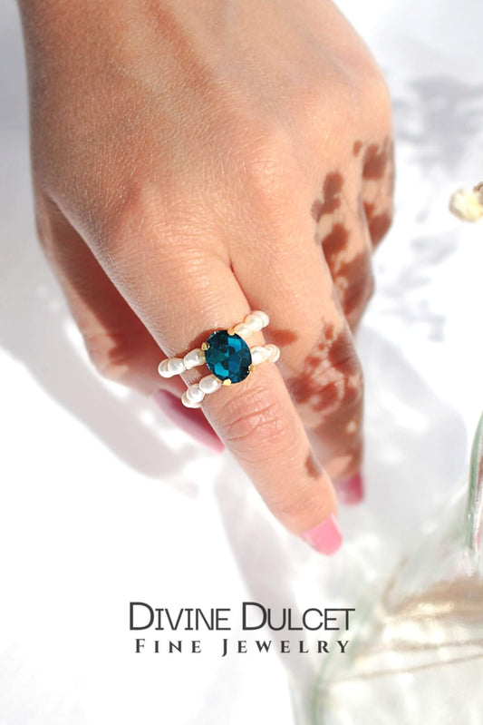Hand wearing a ring with a blue gemstone on a white background, featuring the brand 'Divine Dulcet'.