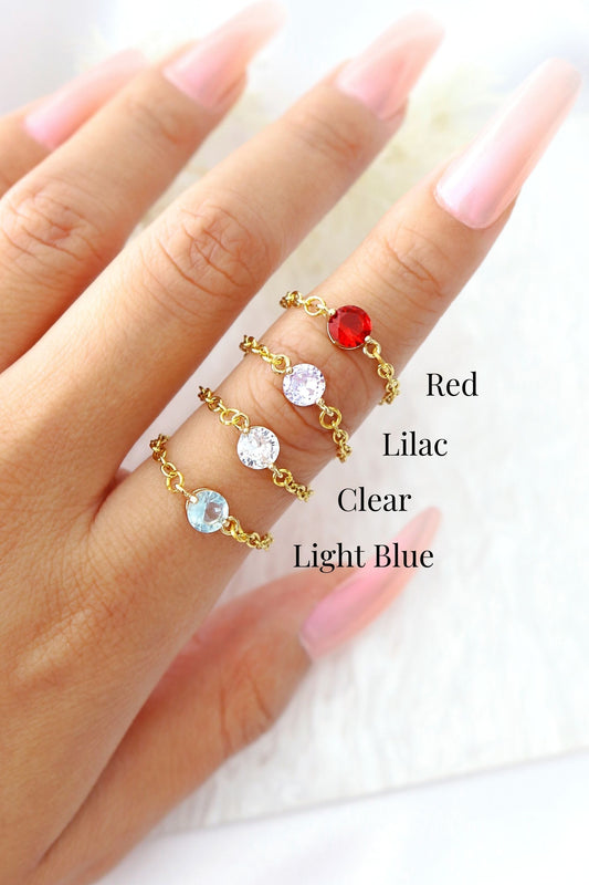 Gold rings with colored stones on a hand, labeled Red, Lilac, Clear, Light Blue.