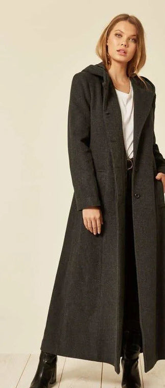 Woman wearing a long dark coat with a plain background