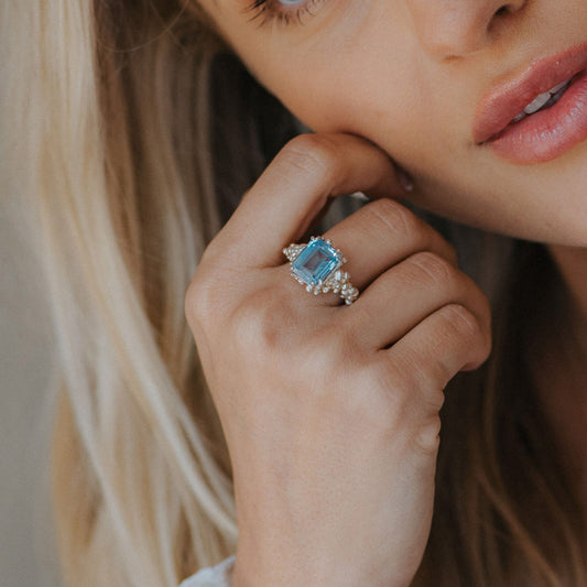 Close-up of a woman's hand wearing a blue gemstone ring with a blurred background