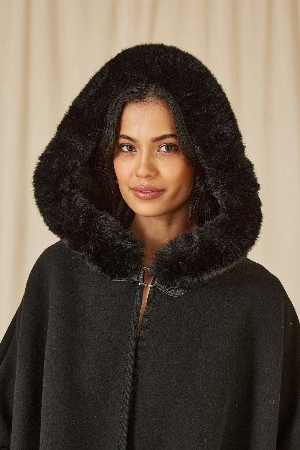 Woman wearing a black coat with a fur-lined hood against a beige background