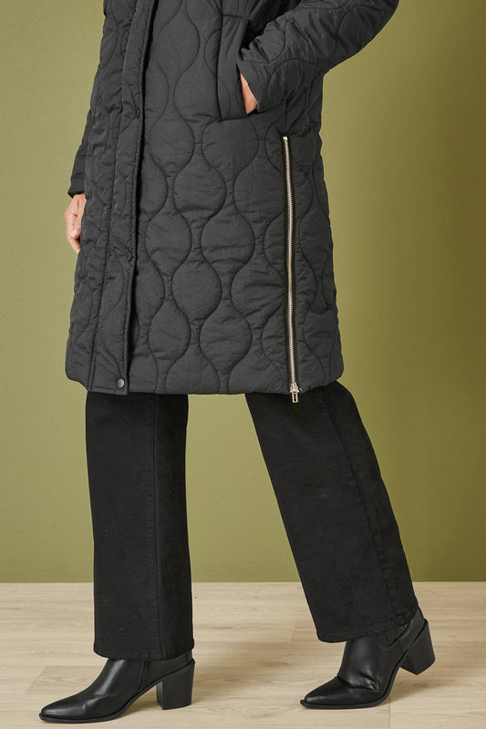 Person wearing a black quilted coat with a green background