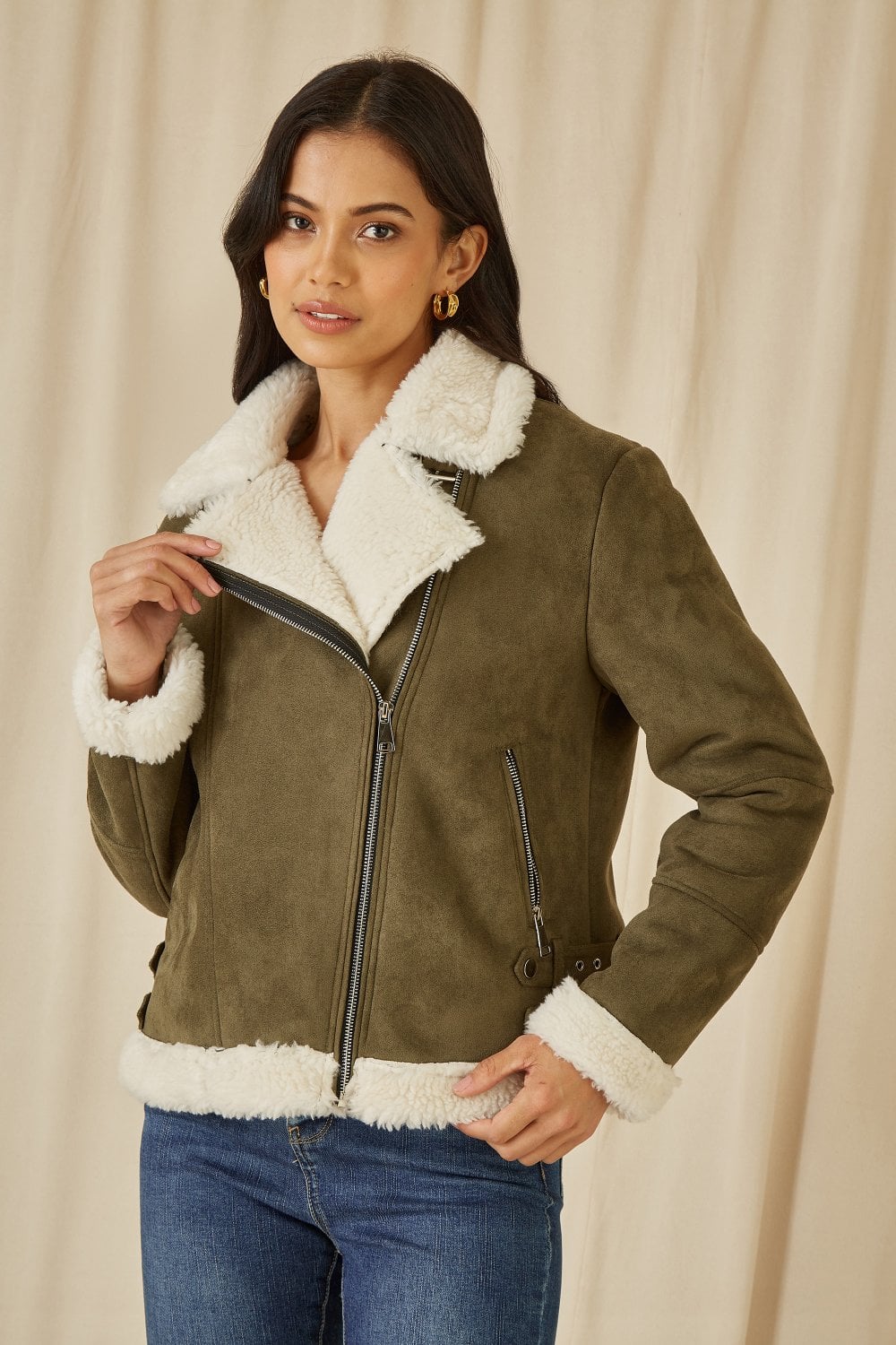 Woman wearing a green suede jacket with white fur trim against a beige background
