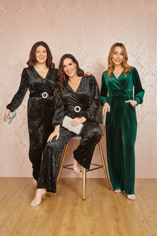 Three women in elegant outfits posing together against a neutral background