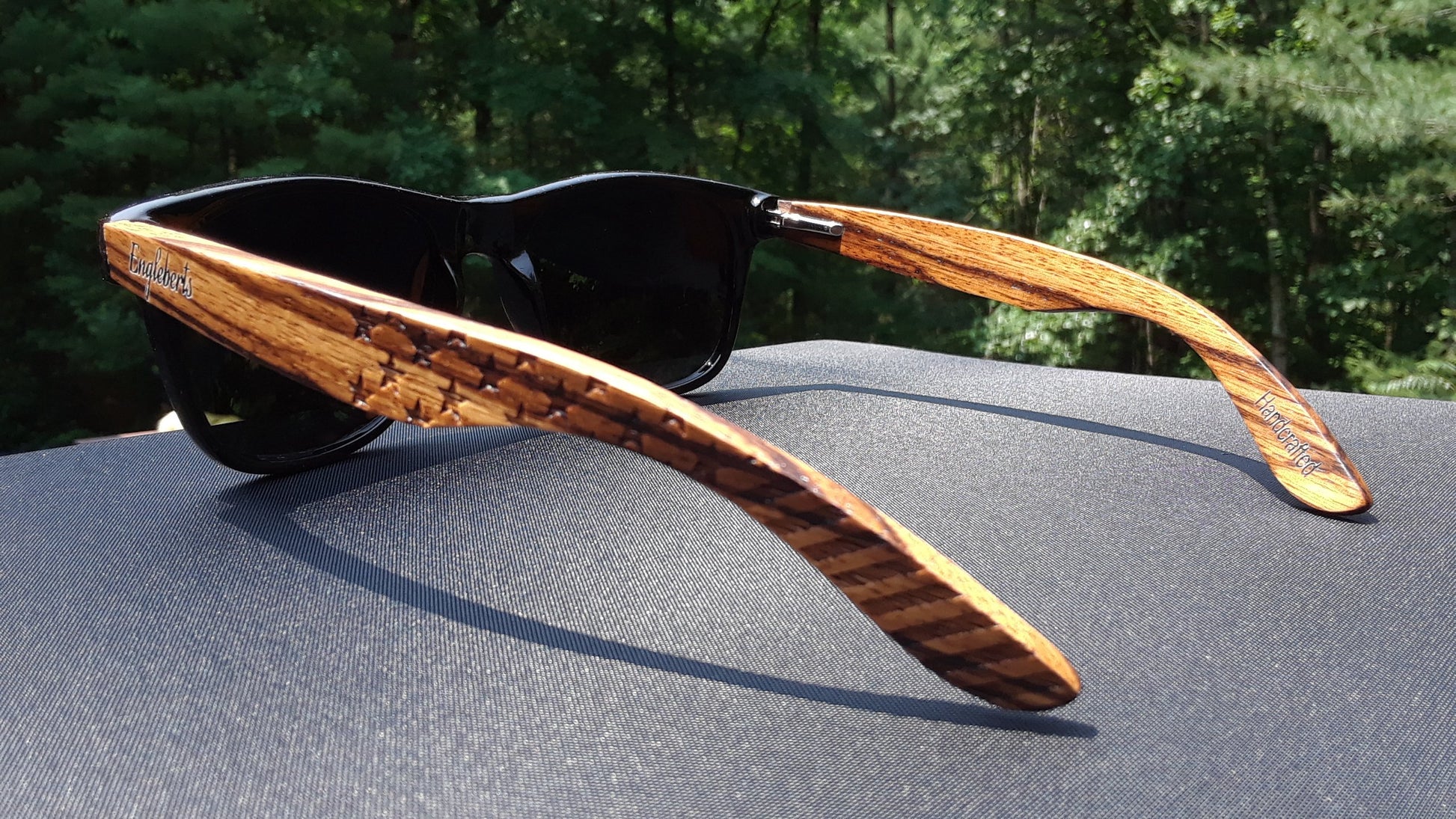 Wooden-framed sunglasses on a car hood with a blurred natural background