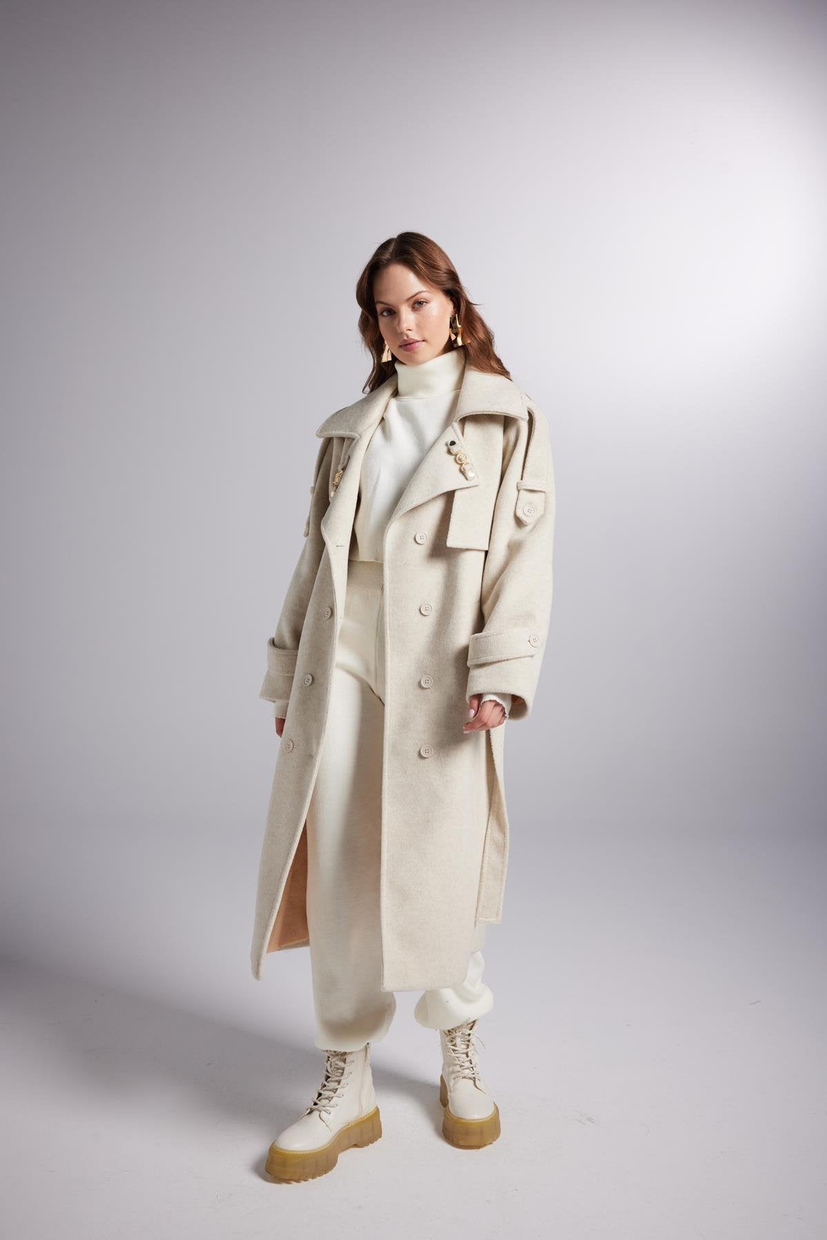Woman wearing a long beige coat on a plain background
