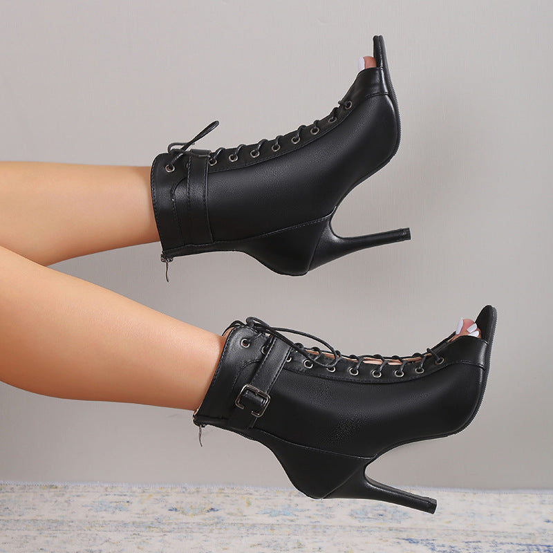 Black high-heeled boots with lace-up design worn by a person on a neutral background