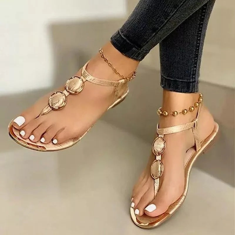 Gold sandals with decorative straps worn with black jeans on a neutral background