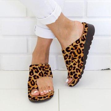 Leopard print sandals worn with white pants on a light wooden floor.