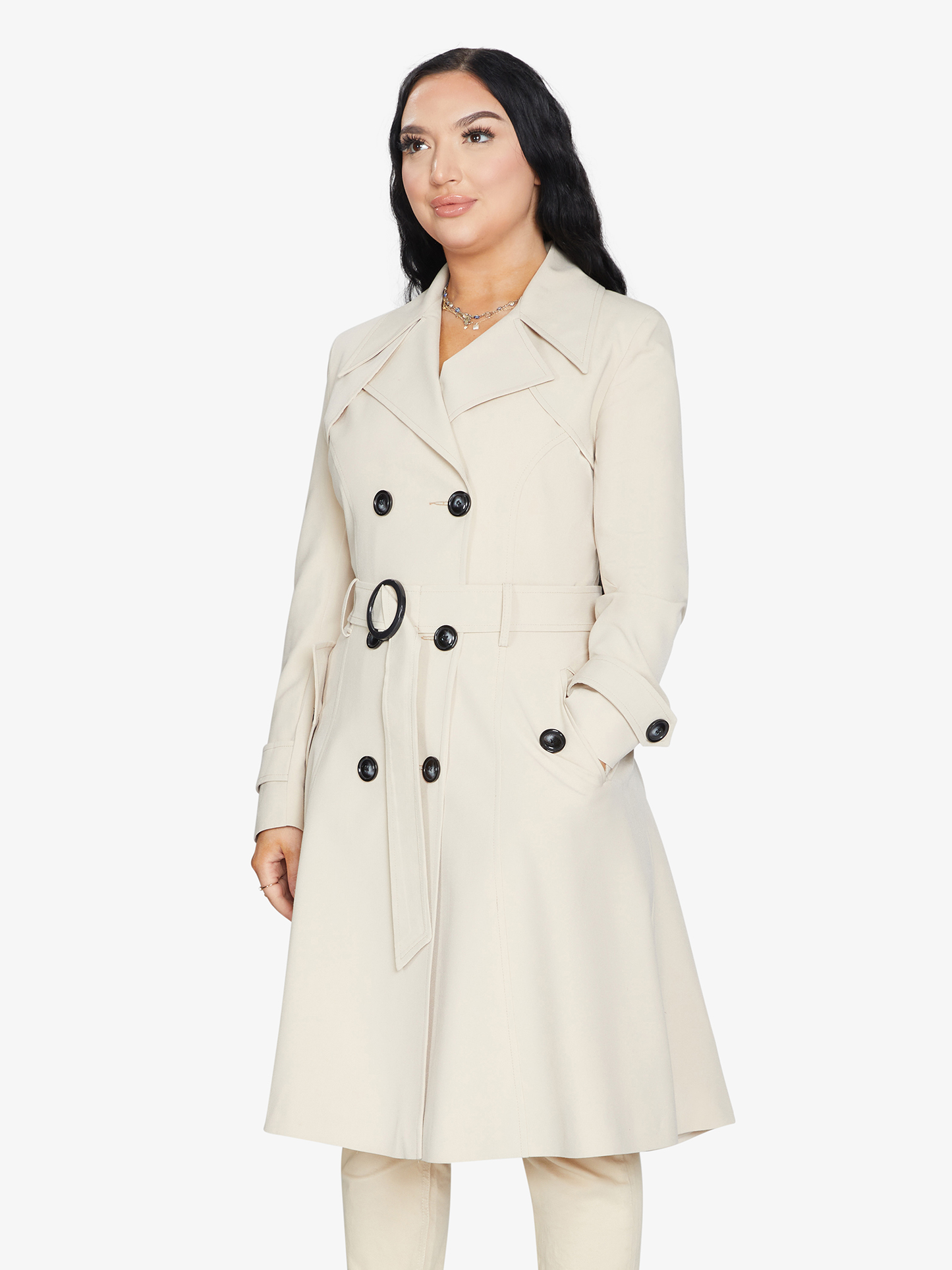 Woman wearing a beige trench coat with black buttons on a white background