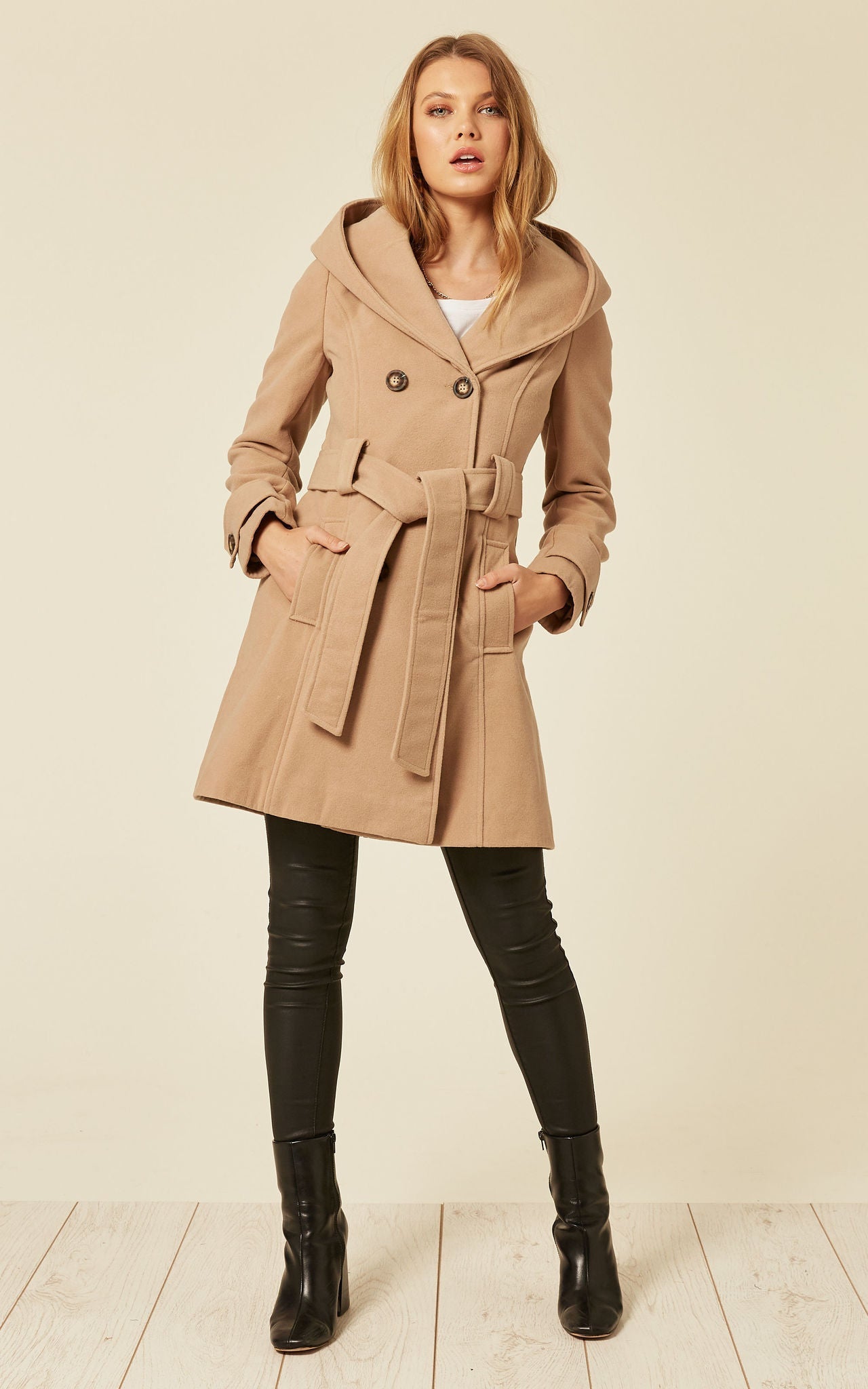 Woman wearing a beige coat with a belt on a plain background
