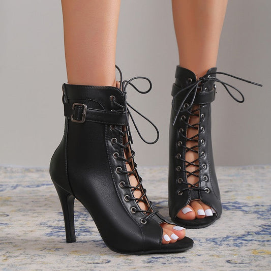 Black lace-up high-heeled shoes worn by a person on a neutral background