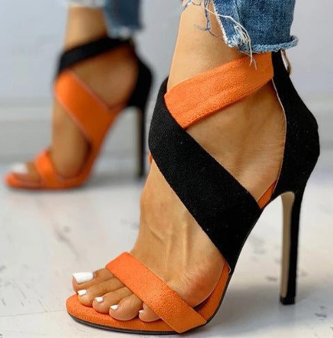 Black and orange high-heeled sandals worn with denim jeans on a light background
