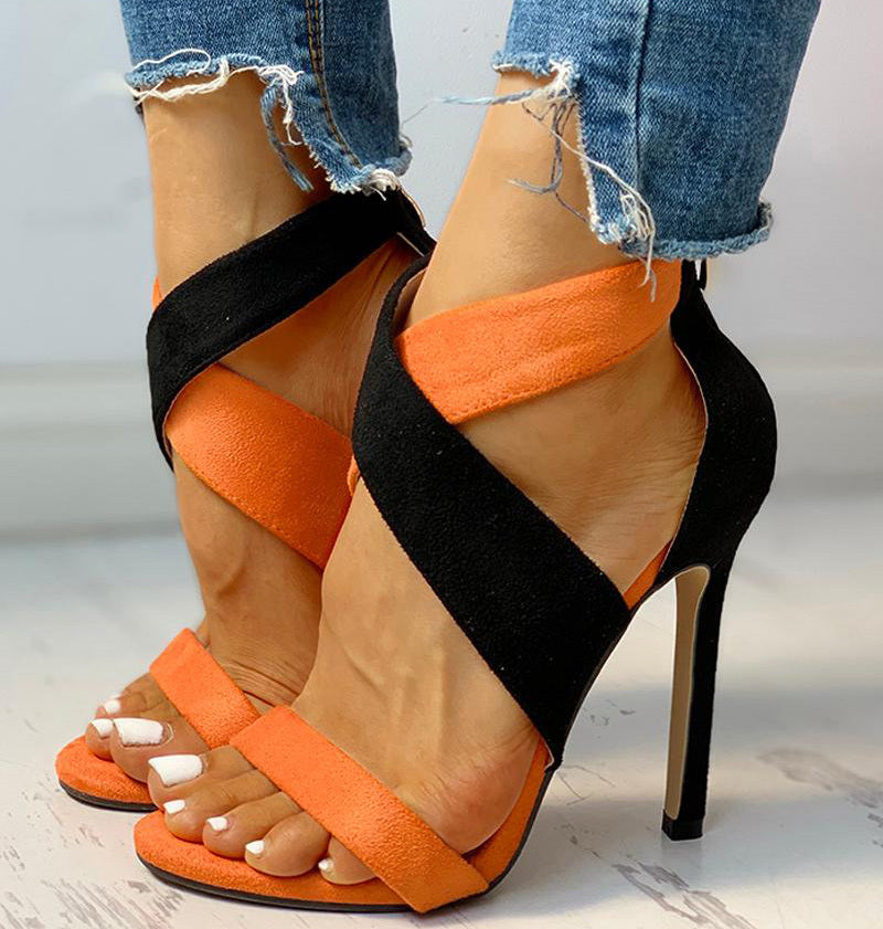 Orange and black high-heeled sandals worn with ripped jeans on a light background