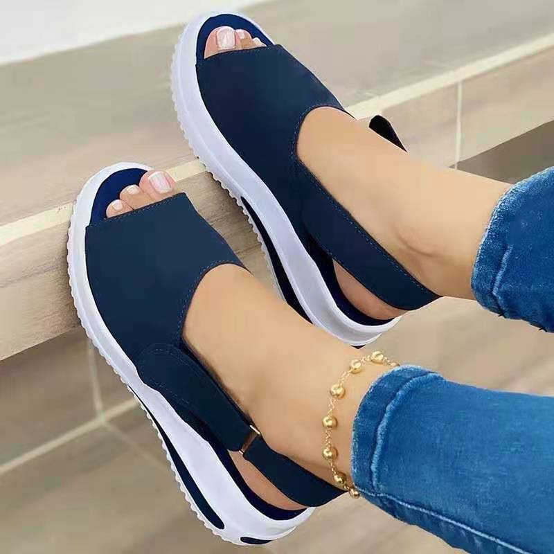 Navy sandals with white soles worn by a person, sitting on a step.