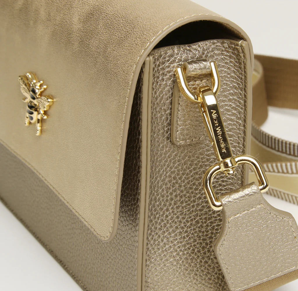 Close-up of a beige handbag with a gold bee emblem and clasp on a light background
